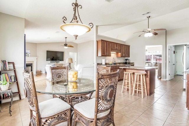 tiled dining room featuring a fireplace, vaulted ceiling, sink, and ceiling fan