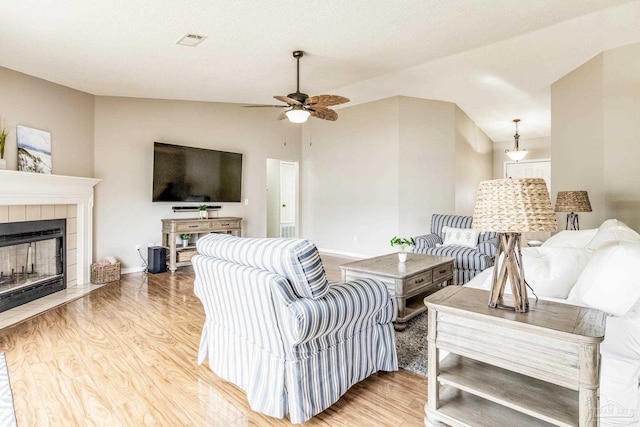 living room featuring vaulted ceiling, light hardwood / wood-style floors, a tile fireplace, and ceiling fan