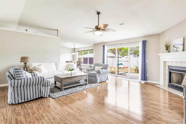 living room with ceiling fan, a tile fireplace, light hardwood / wood-style flooring, and a textured ceiling