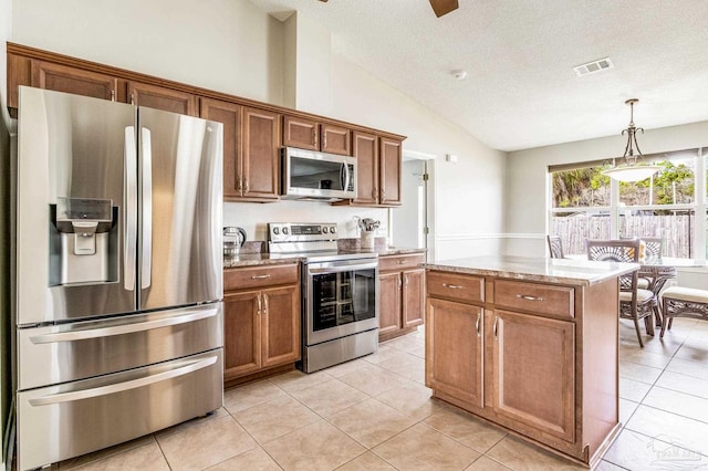 kitchen with stainless steel appliances, a textured ceiling, a kitchen island, decorative light fixtures, and vaulted ceiling