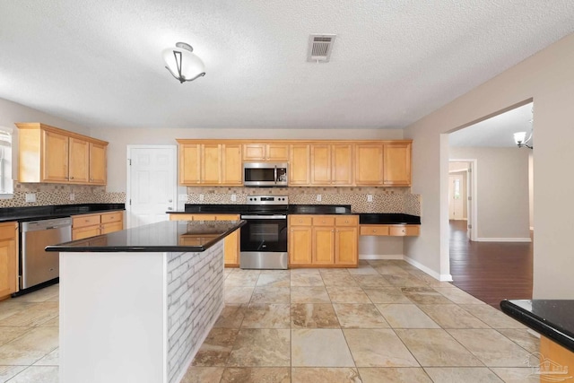 kitchen featuring appliances with stainless steel finishes, light brown cabinetry, tasteful backsplash, a textured ceiling, and a center island