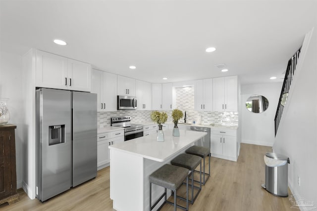 kitchen featuring white cabinetry, light wood-type flooring, appliances with stainless steel finishes, a kitchen breakfast bar, and a kitchen island