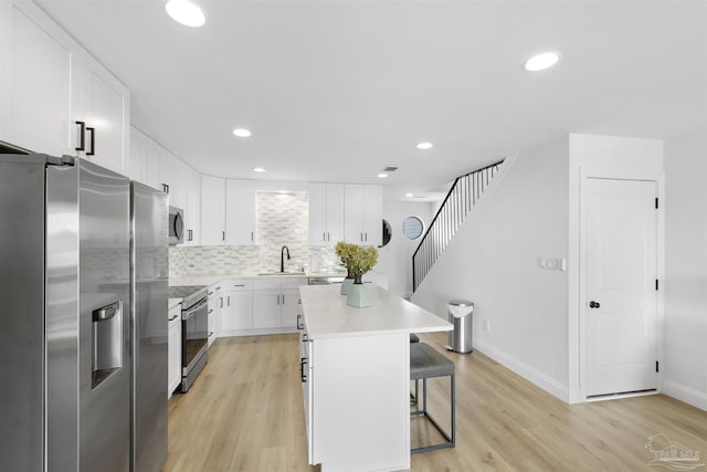 kitchen featuring white cabinetry, tasteful backsplash, a center island, a kitchen breakfast bar, and stainless steel appliances