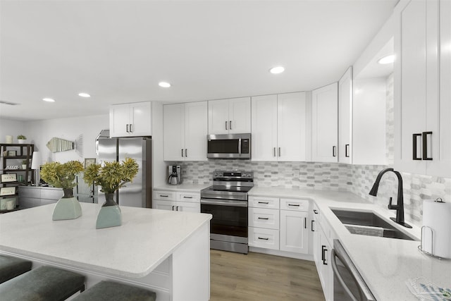 kitchen with stainless steel appliances, white cabinetry, sink, and a kitchen bar