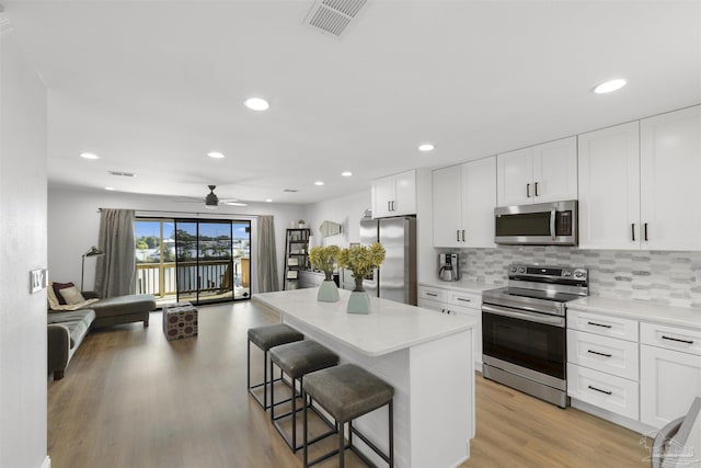 kitchen featuring stainless steel appliances, a kitchen island, white cabinets, and a kitchen bar