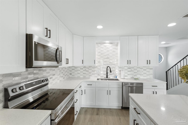 kitchen with sink, white cabinetry, stainless steel appliances, light hardwood / wood-style floors, and backsplash