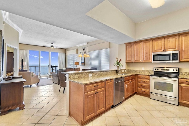 kitchen featuring light stone countertops, a peninsula, a sink, appliances with stainless steel finishes, and brown cabinets