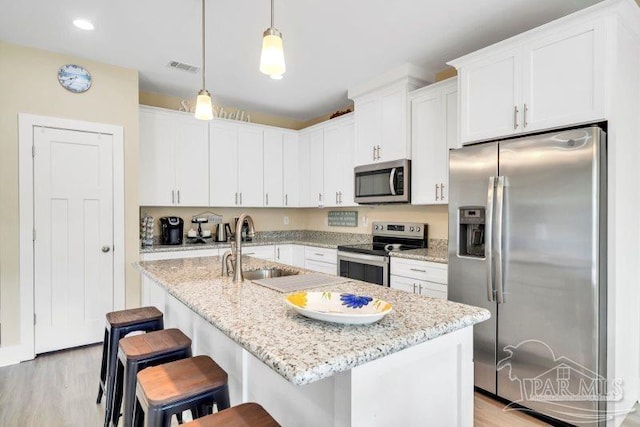 kitchen with sink, appliances with stainless steel finishes, an island with sink, white cabinets, and light wood-type flooring