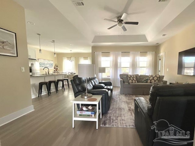 living room featuring ceiling fan with notable chandelier, dark hardwood / wood-style flooring, sink, and a tray ceiling