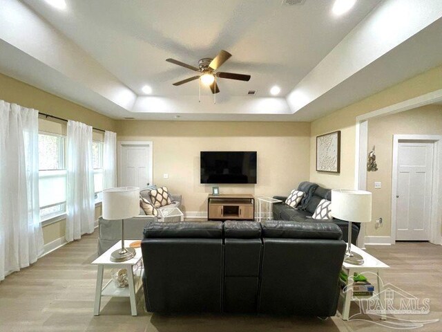 living room with ceiling fan, a raised ceiling, and light hardwood / wood-style flooring