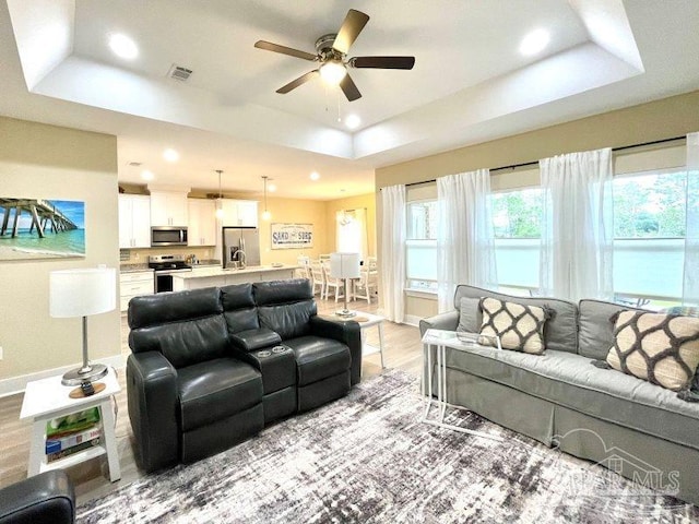 living room featuring light hardwood / wood-style floors, a raised ceiling, and ceiling fan