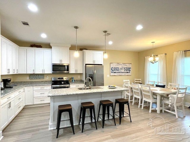 kitchen featuring pendant lighting, an island with sink, appliances with stainless steel finishes, and light hardwood / wood-style flooring