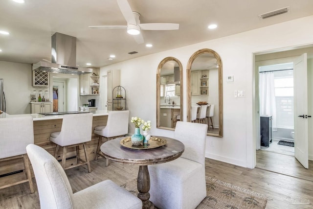 dining area with ceiling fan, wet bar, and light wood-type flooring