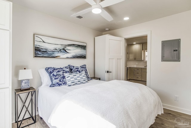 bedroom featuring connected bathroom, hardwood / wood-style flooring, electric panel, and ceiling fan