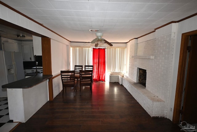 dining room with visible vents, a ceiling fan, ornamental molding, dark wood-style flooring, and a brick fireplace