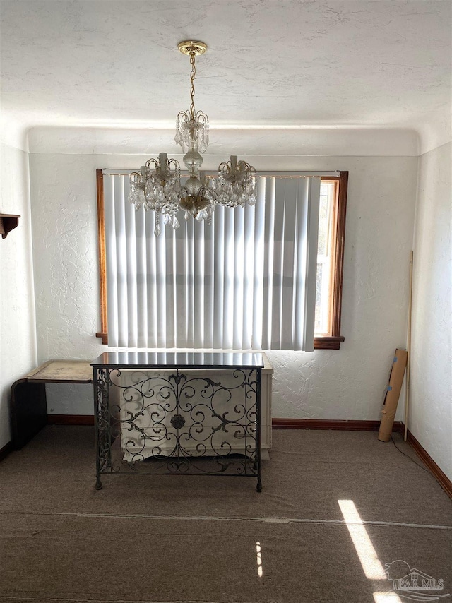 empty room with a chandelier, a textured wall, carpet flooring, and baseboards