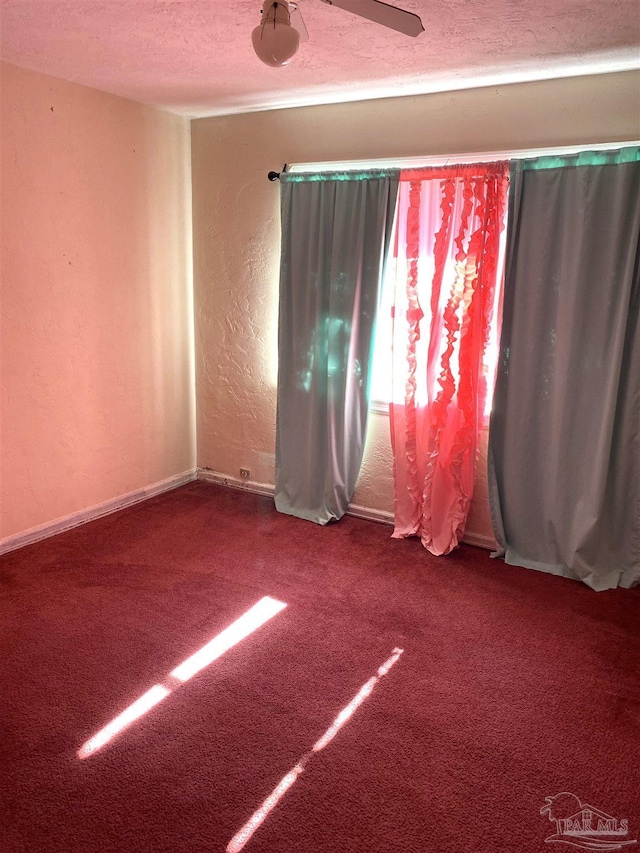 carpeted empty room with a textured wall, a textured ceiling, and baseboards