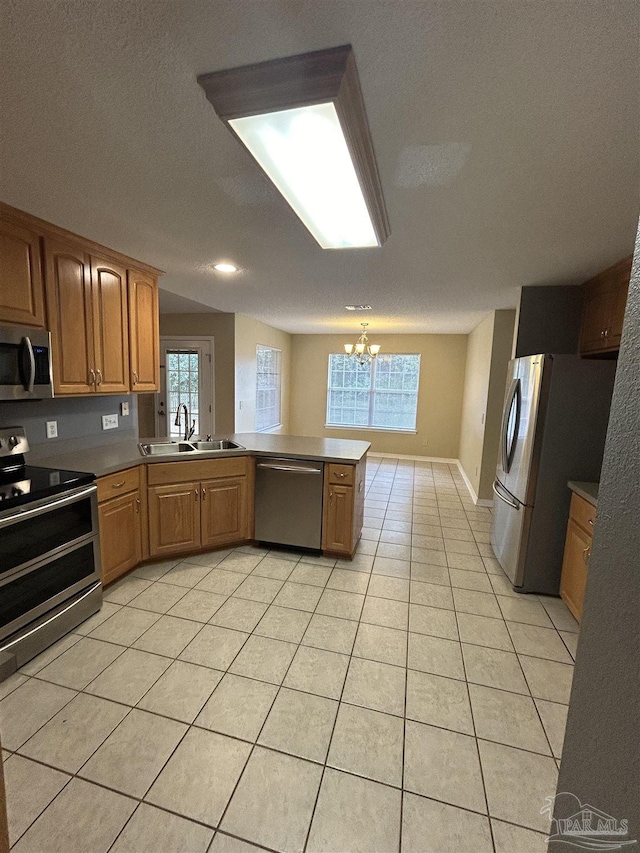 kitchen featuring kitchen peninsula, appliances with stainless steel finishes, sink, an inviting chandelier, and light tile patterned flooring