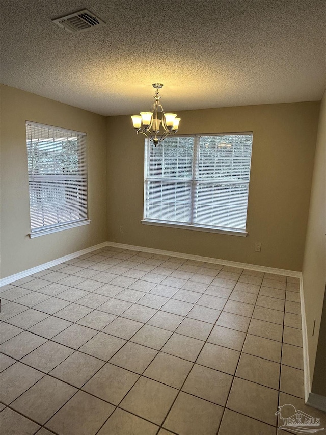 tiled spare room featuring a textured ceiling, a healthy amount of sunlight, and a notable chandelier