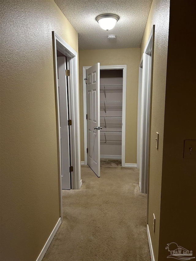 corridor with light colored carpet and a textured ceiling