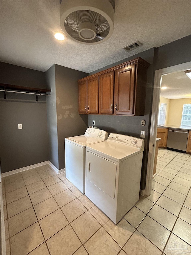 laundry room with cabinets, light tile patterned floors, a textured ceiling, and washing machine and clothes dryer