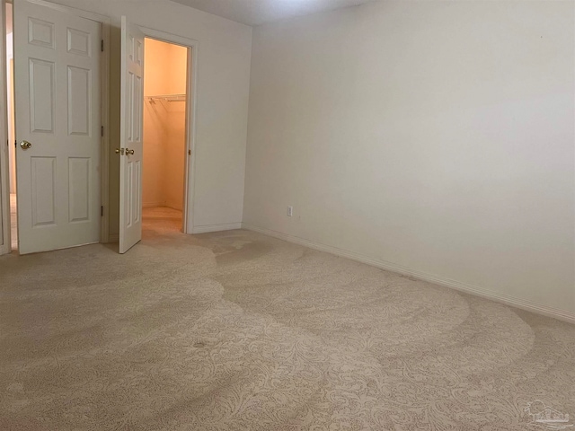 unfurnished bedroom featuring a walk in closet, light colored carpet, and a closet