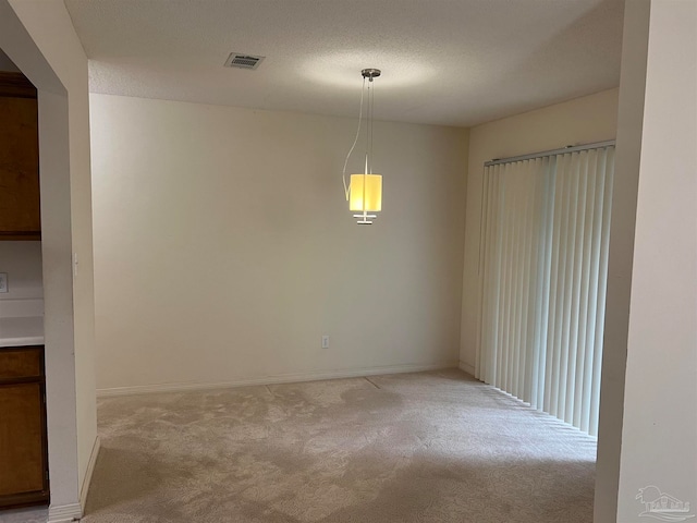 unfurnished dining area featuring a textured ceiling and light colored carpet