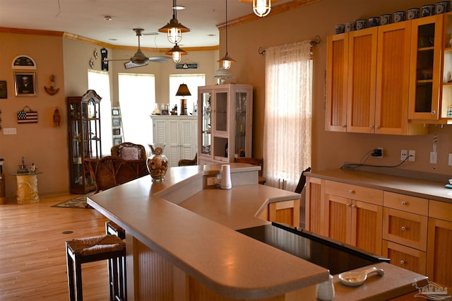 kitchen with decorative light fixtures, ornamental molding, a kitchen bar, a kitchen island, and light hardwood / wood-style flooring