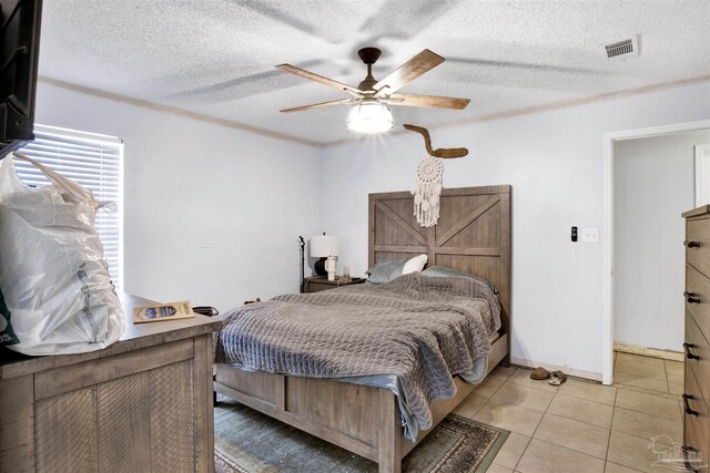 bedroom featuring ornamental molding, light tile patterned floors, a textured ceiling, ensuite bathroom, and ceiling fan