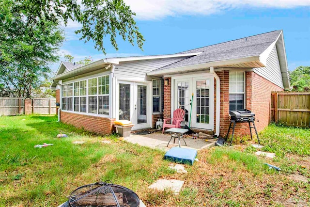 back of property with a fire pit, a lawn, and a sunroom