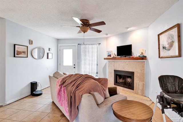 living room featuring a textured ceiling, light tile patterned flooring, a fireplace, and ceiling fan