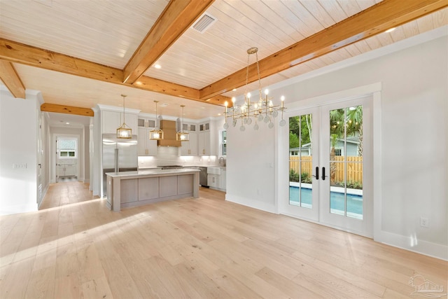 unfurnished living room with beamed ceiling, a notable chandelier, light wood-type flooring, and french doors