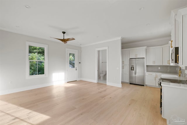 kitchen featuring crown molding, light hardwood / wood-style flooring, appliances with stainless steel finishes, white cabinetry, and tasteful backsplash