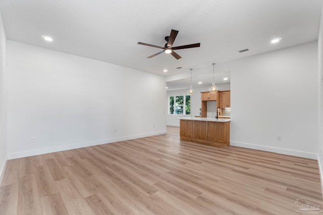 unfurnished living room with light hardwood / wood-style floors, sink, and ceiling fan