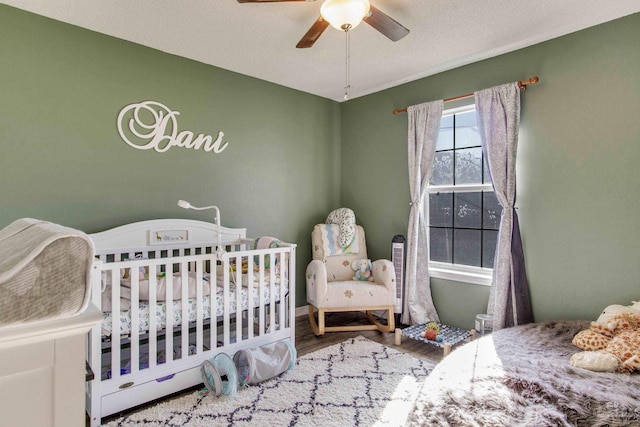 bedroom with a textured ceiling, a crib, wood-type flooring, and ceiling fan