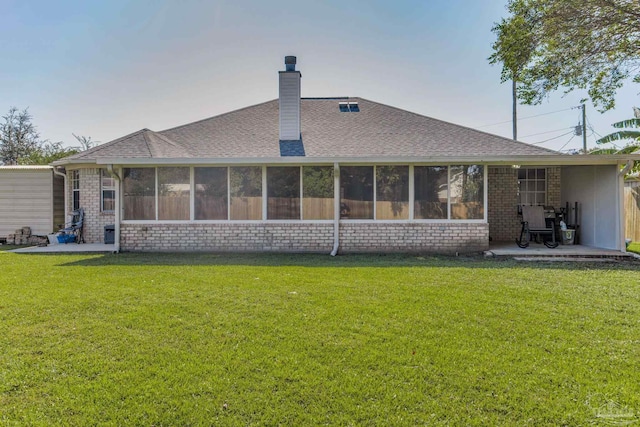 back of property with a sunroom, a lawn, and a patio area