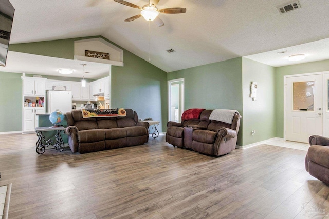 living room featuring ceiling fan, vaulted ceiling, light hardwood / wood-style floors, and a textured ceiling