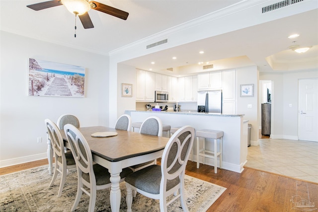 dining room featuring baseboards, light wood finished floors, visible vents, and crown molding