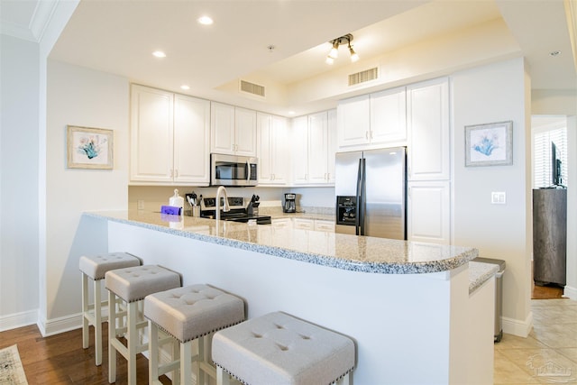 kitchen featuring a peninsula, visible vents, stainless steel appliances, and a kitchen breakfast bar