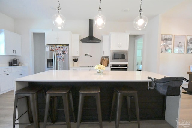 kitchen featuring appliances with stainless steel finishes, a large island, white cabinetry, light hardwood / wood-style flooring, and wall chimney exhaust hood