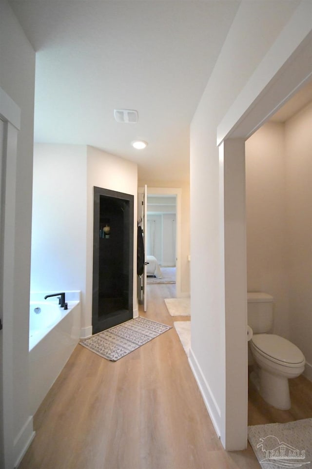 bathroom with a tub to relax in, toilet, and hardwood / wood-style floors