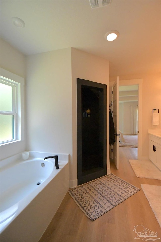 bathroom featuring wood-type flooring, vanity, and a tub to relax in