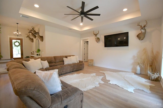 living room with light hardwood / wood-style floors, ceiling fan with notable chandelier, and a raised ceiling