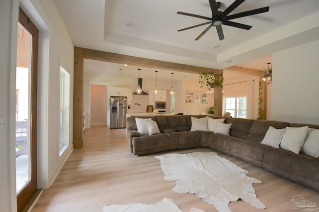 living room featuring ceiling fan, light wood-type flooring, and a tray ceiling