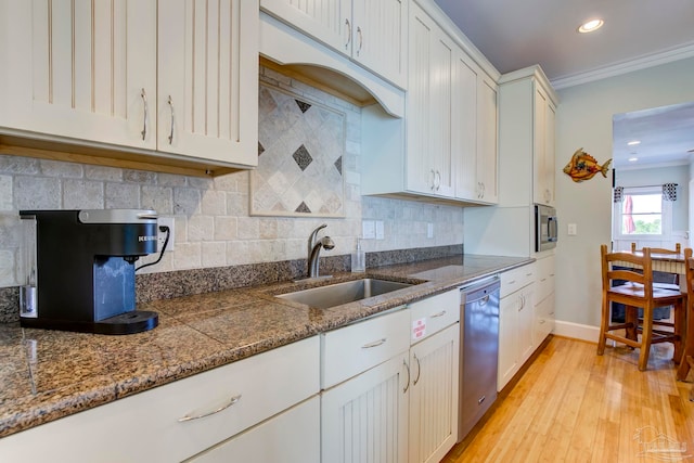 kitchen with white cabinets, ornamental molding, sink, stainless steel appliances, and light wood-type flooring