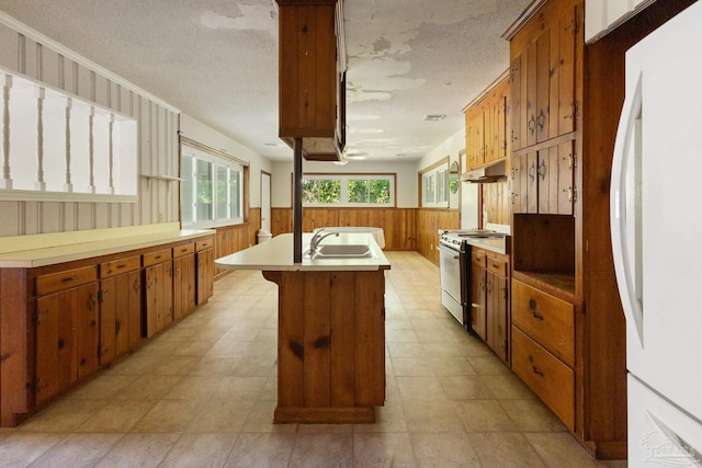 kitchen featuring sink, stainless steel stove, white refrigerator, an island with sink, and a textured ceiling