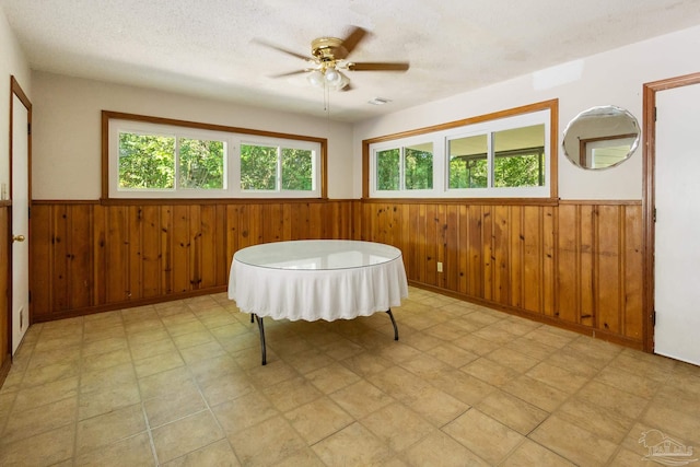 living area with ceiling fan, a textured ceiling, and wood walls