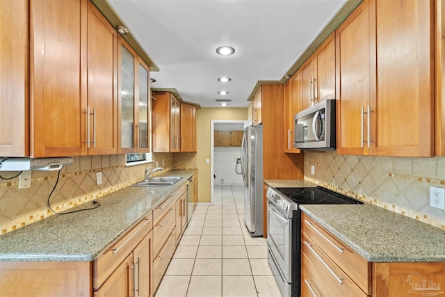 kitchen featuring sink, light tile patterned floors, stainless steel appliances, light stone countertops, and decorative backsplash