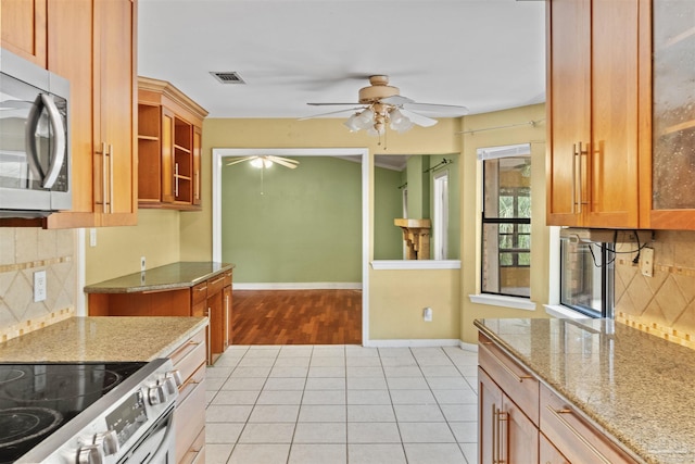 kitchen with light tile patterned floors, ceiling fan, stainless steel appliances, light stone countertops, and backsplash