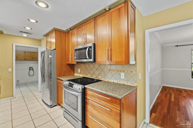 kitchen featuring light stone counters, appliances with stainless steel finishes, light tile patterned floors, and backsplash